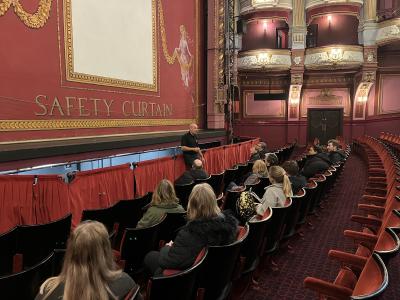 A group of people sat in a theatre auditorium listening to a man give a talk by the stage.